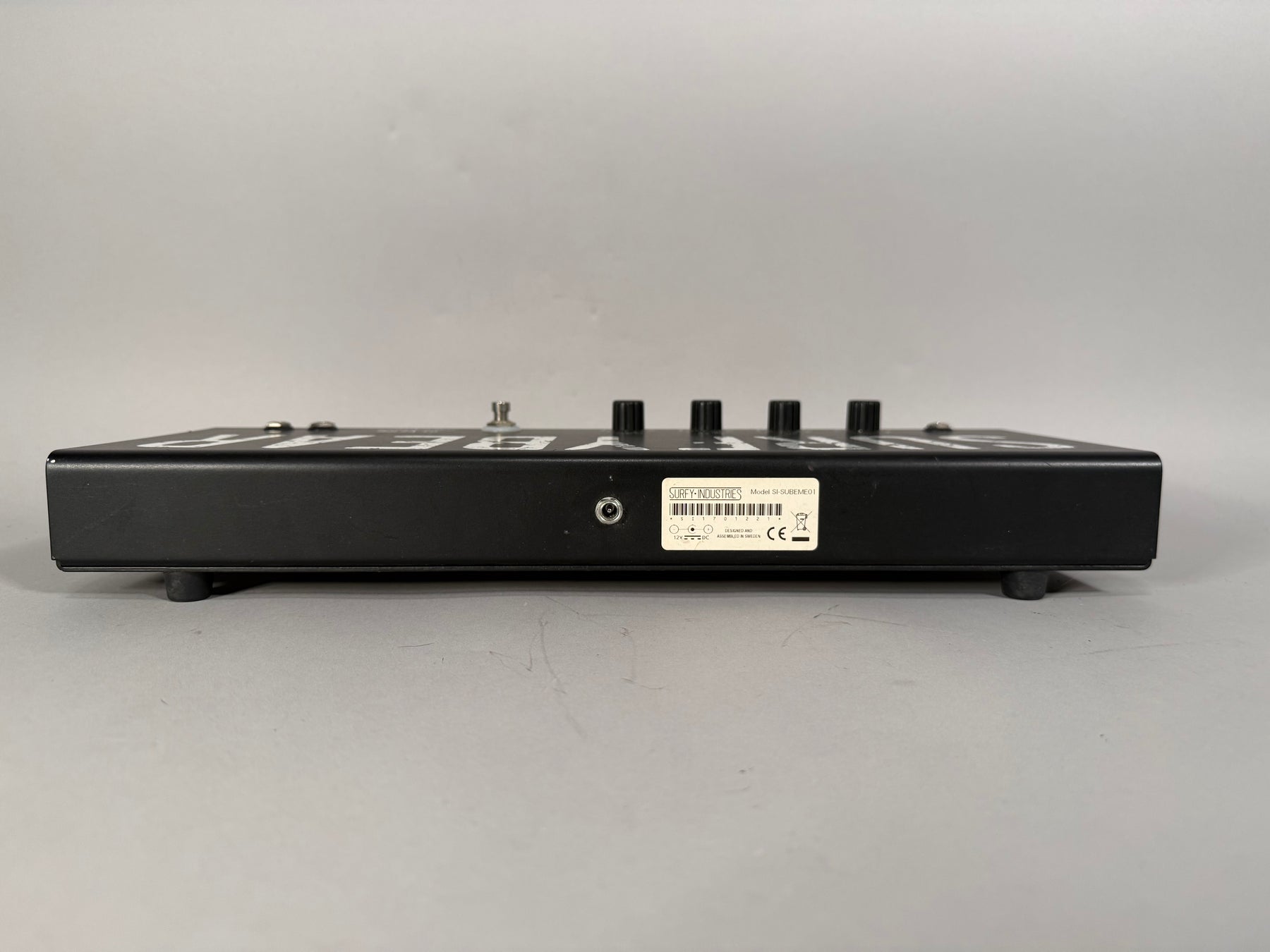 The black metal effects pedal is viewed from the side, showing a power input jack and a white label with black text.