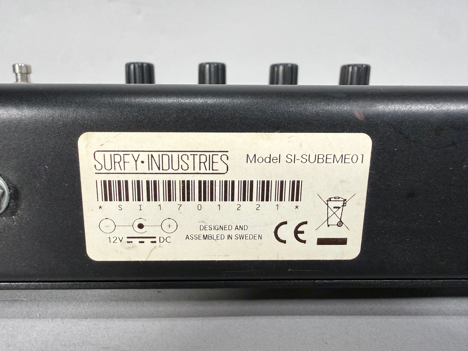 Close-up of the black pedal's rear, showing a white label with a barcode, 12V DC input, and a small red scuff mark.