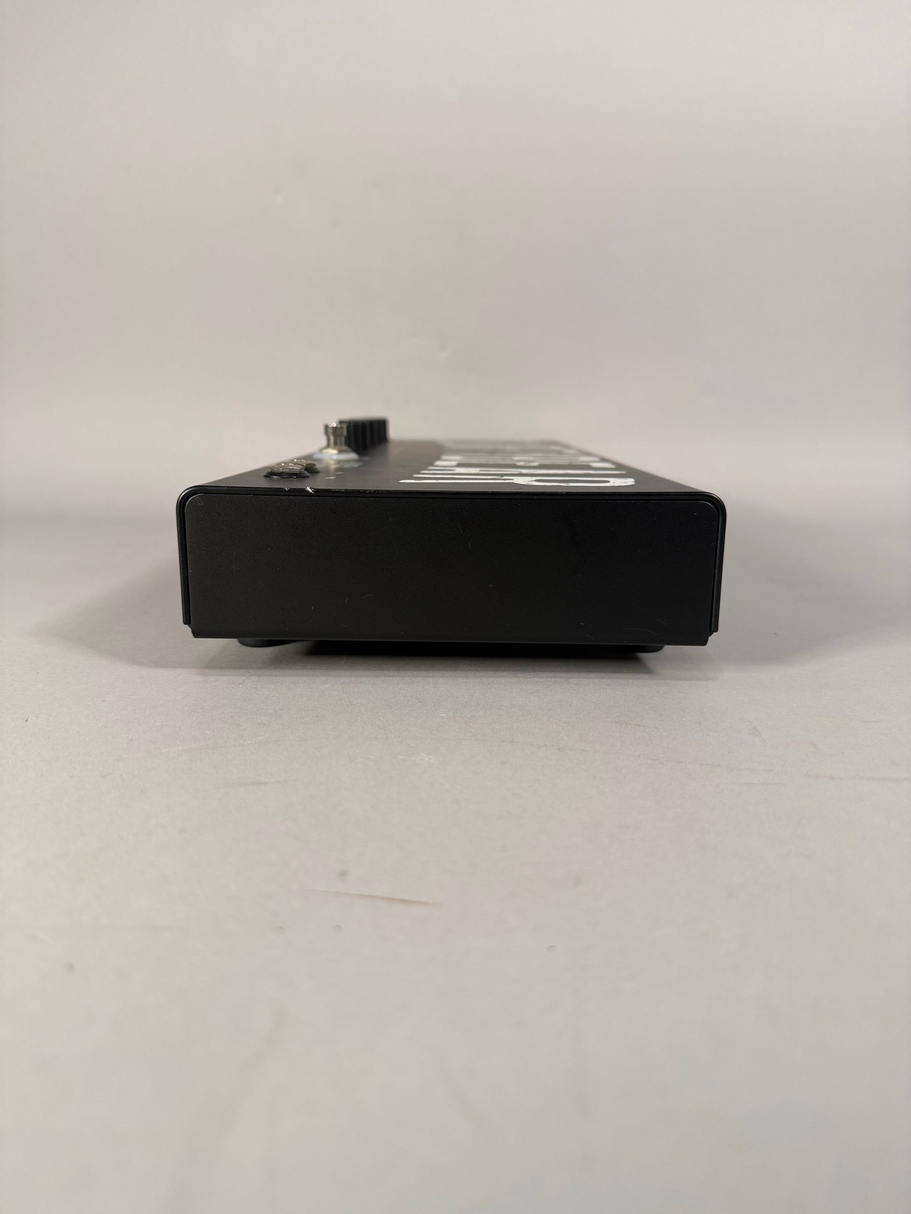 The black metal pedal is viewed from the side, showing a single silver knob and a small silver switch on the top left edge.