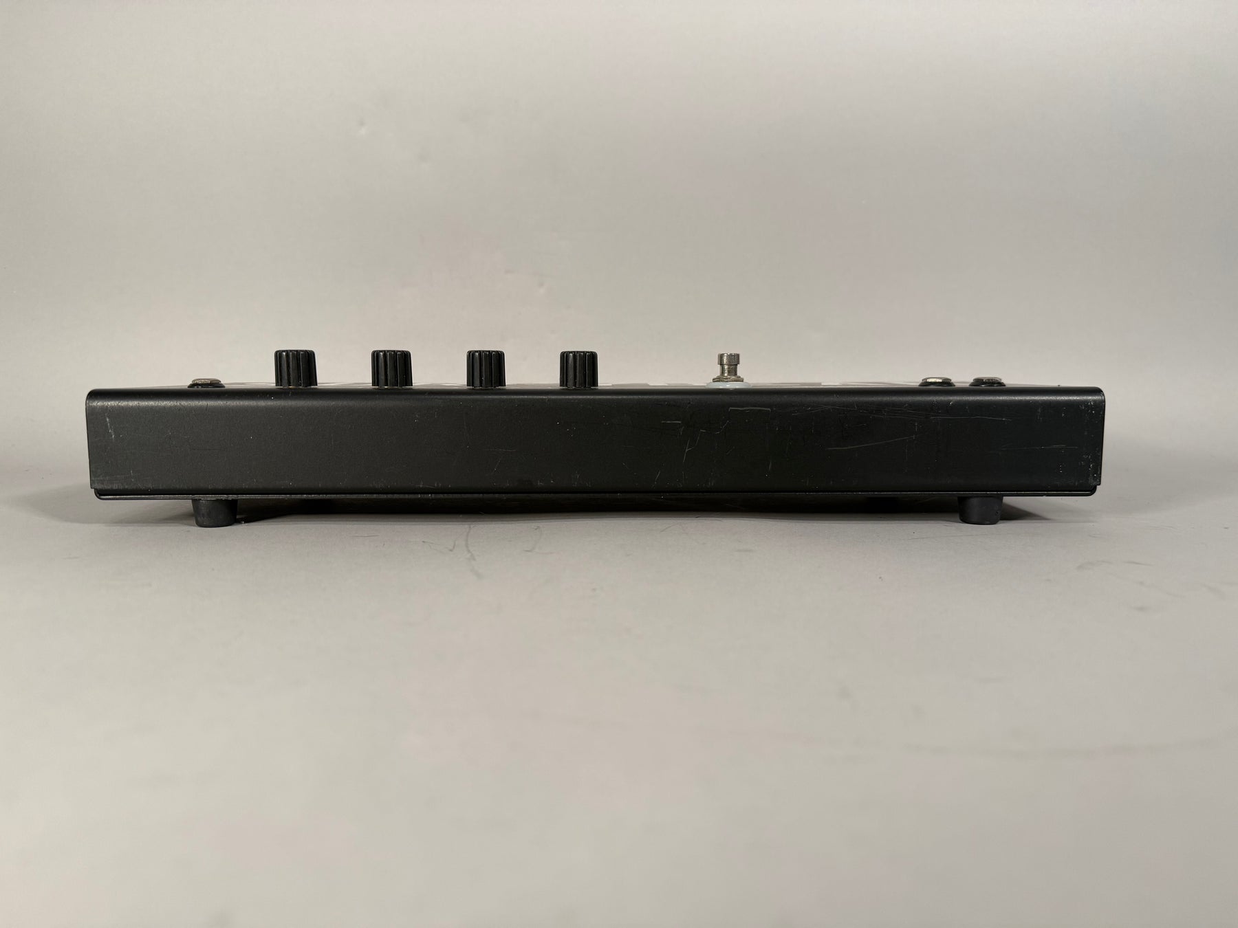 Side view of the black metal pedal, showing four black knobs, a footswitch, and light scuffs on the finish.