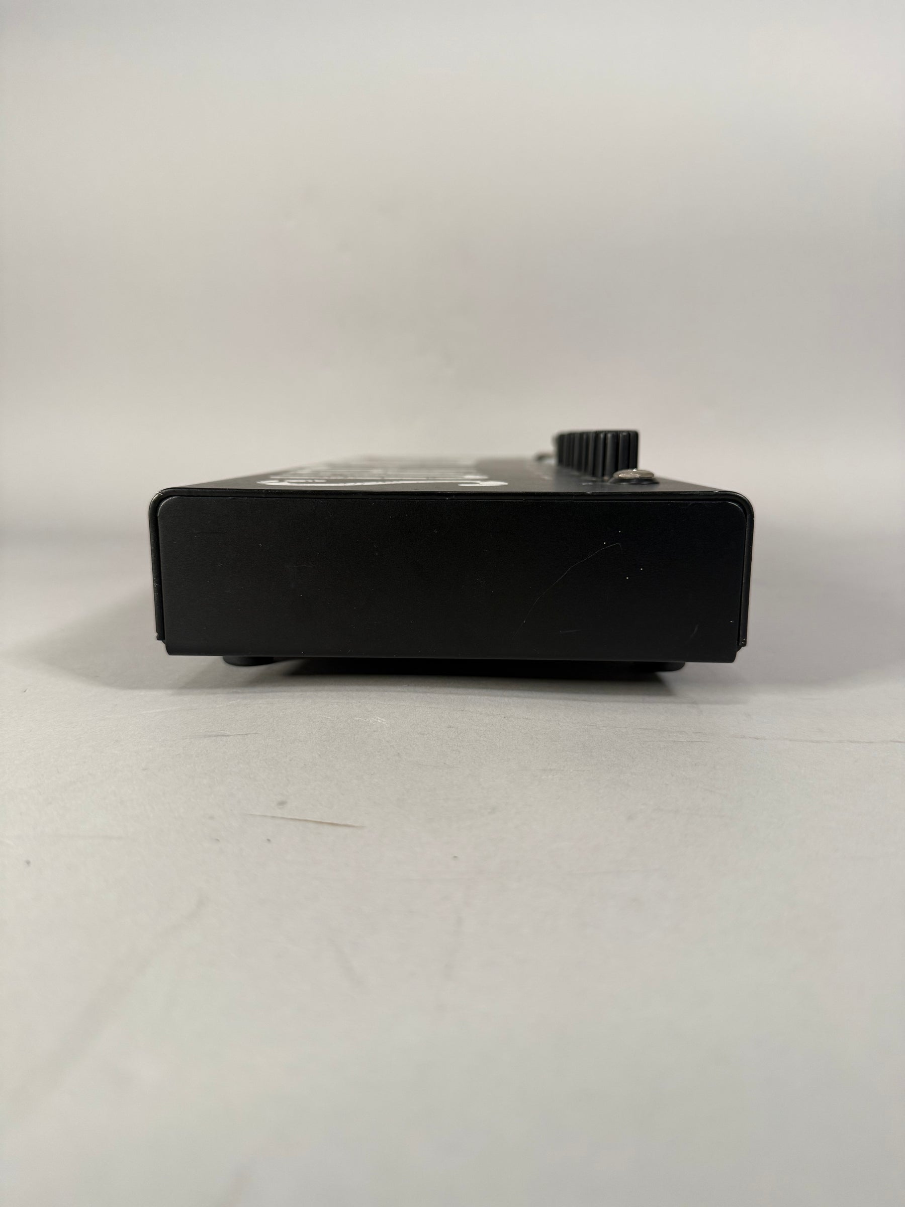 The black metal pedal is viewed from the right side, showing a single ribbed control knob and light surface scratches.