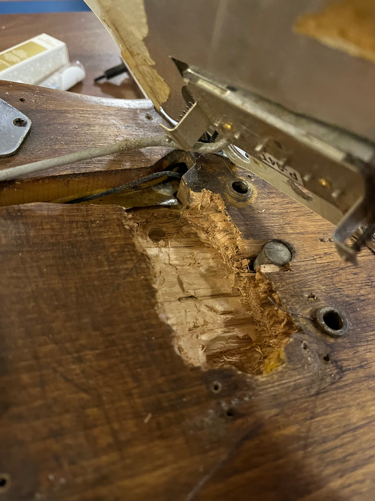 Close-up of the guitar's dark wood body, showing a large, rough cavity carved into the wood, with wires and metal hardware visible.