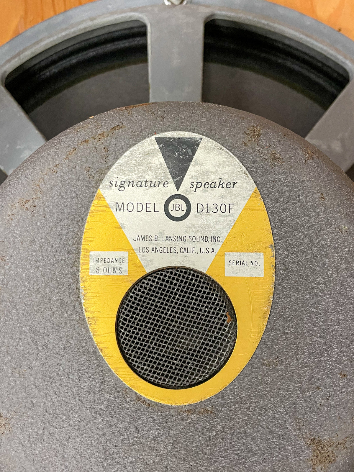 Close-up of the speaker's gray textured dust cap, showing a worn yellow and white label with a black mesh center.