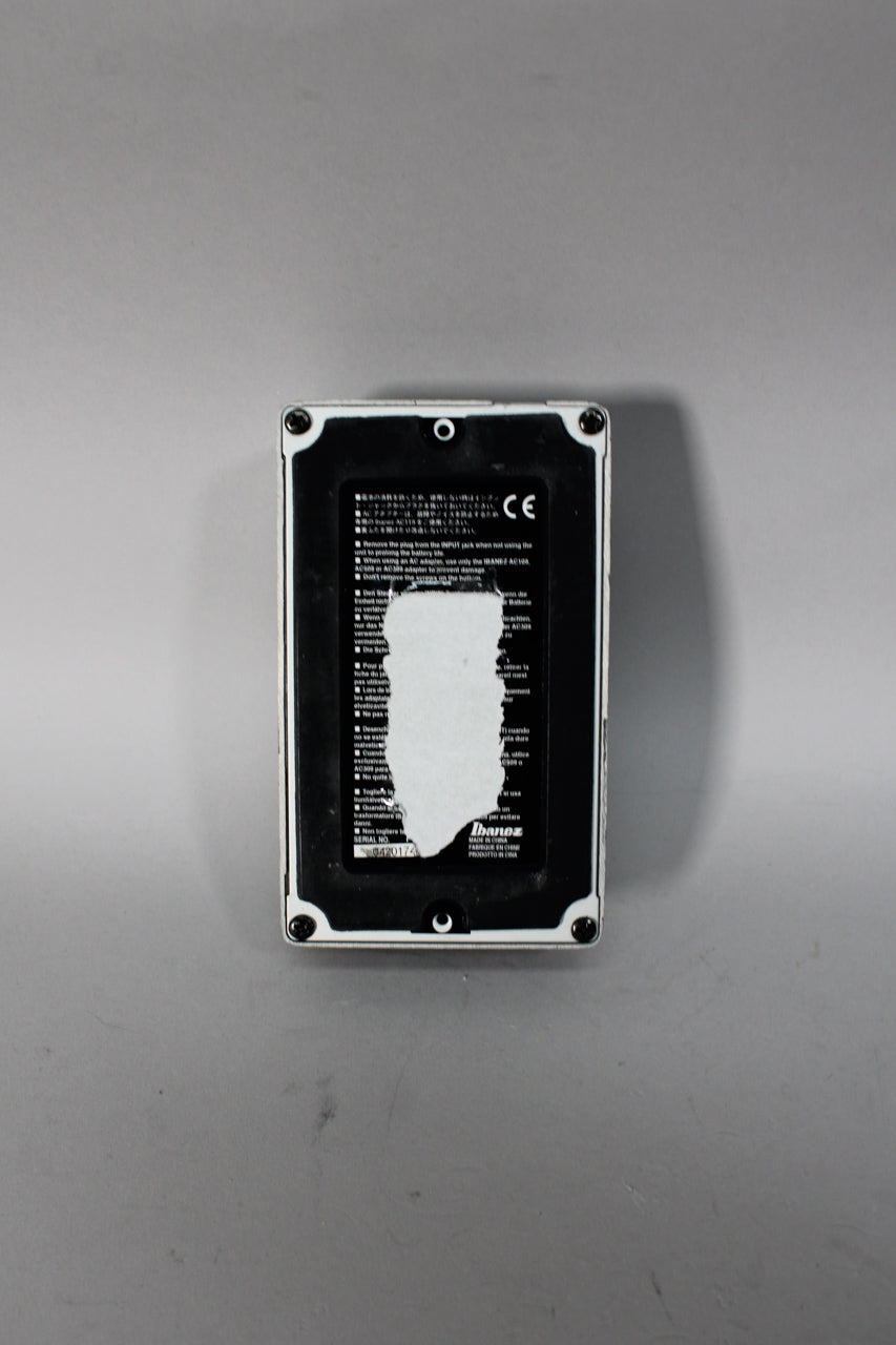 The pedal's black base plate, with a large white sticker residue, is framed by a white casing with four visible screws.