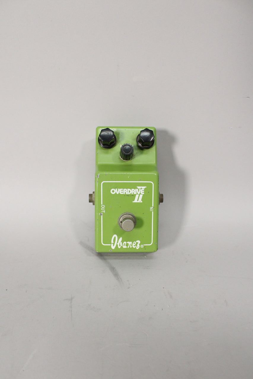 A top-down view of a lime green guitar pedal with three black knobs, a silver footswitch, and visible paint chips.