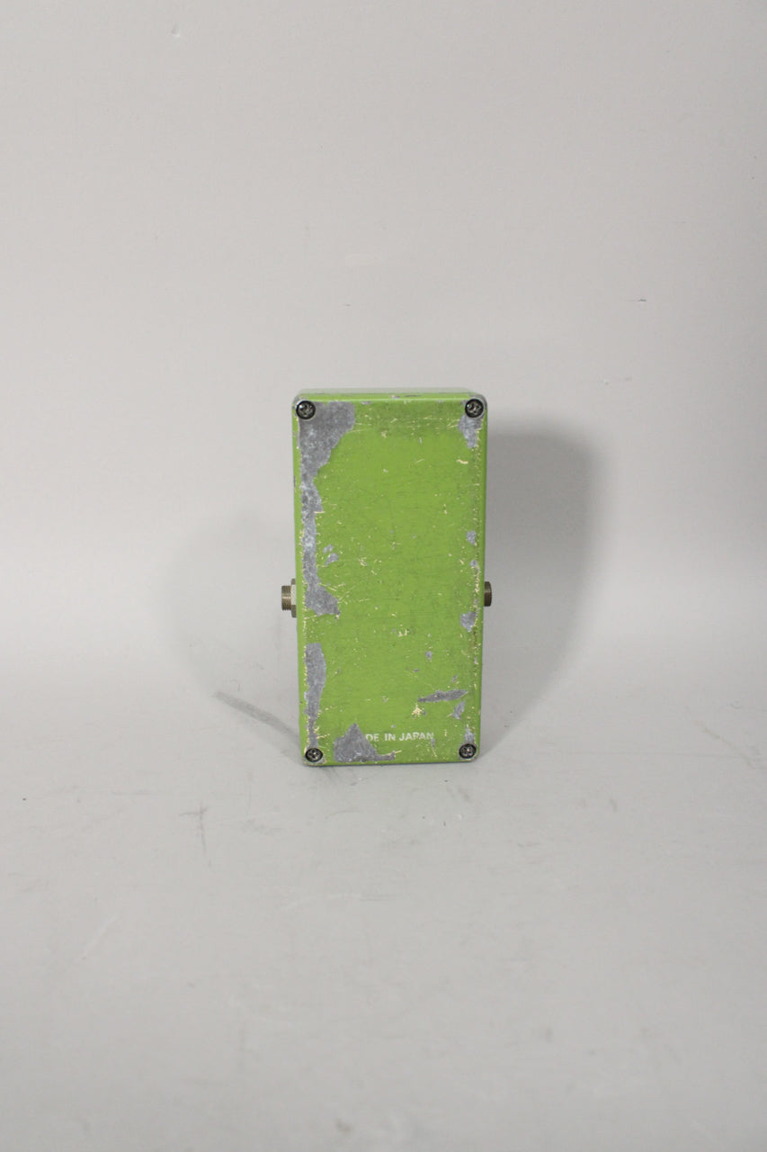 Rear view of a lime green pedal with significant paint chipping revealing silver metal, and four visible screws.