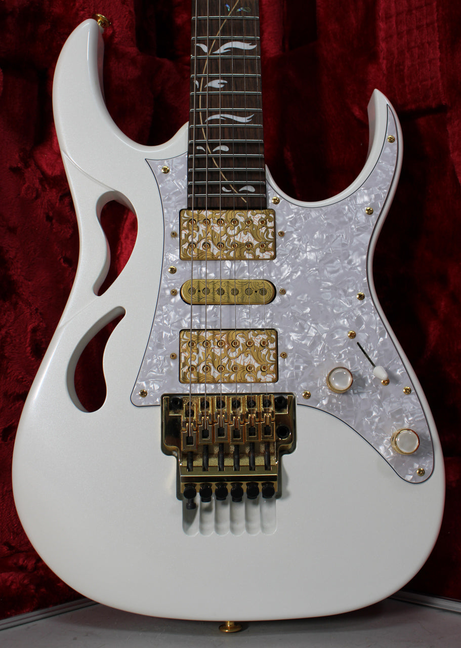The white electric guitar's body, with two "monkey grip" cutouts, features a pearloid pickguard, gold hardware, and ornate gold pickup covers.
