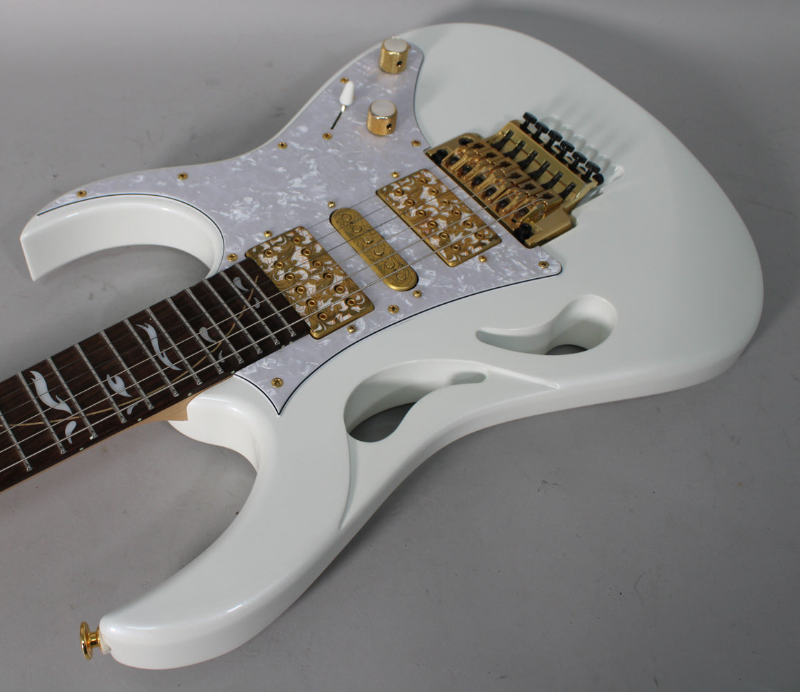 White electric guitar, angled from above, showing its pearloid pickguard, gold hardware, and ornate gold pickup covers.