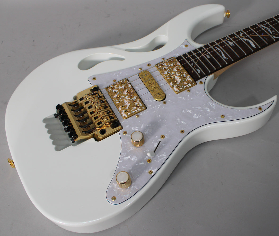 White electric guitar with a pearloid pickguard, gold hardware, and ornate gold pickups, viewed from the upper body.