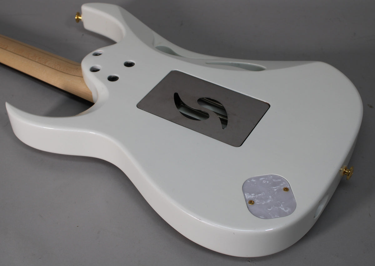 The back of a glossy white electric guitar, angled to show the tremolo cavity with springs, a pearloid control cover, and a natural wood neck.