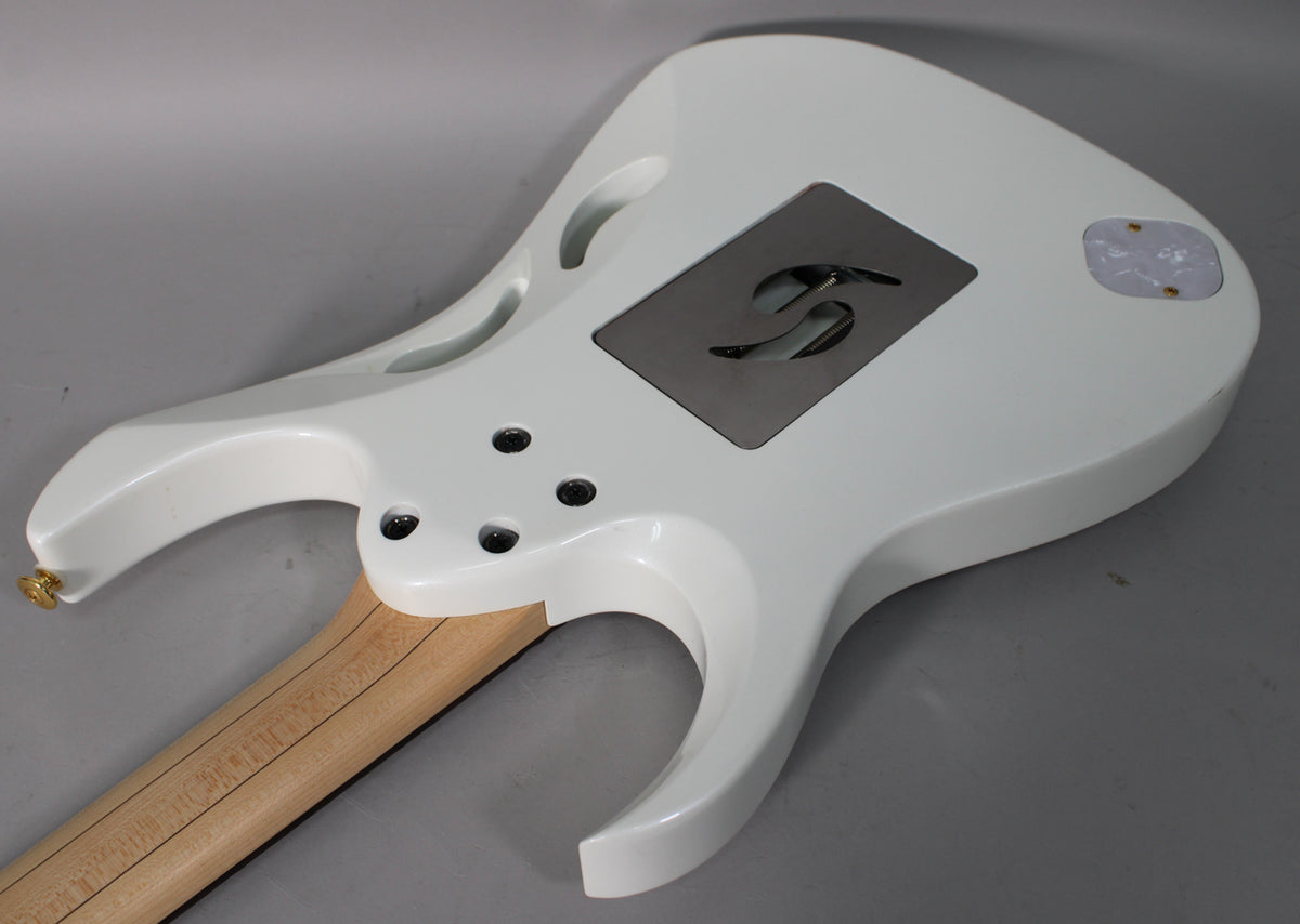 The back of a glossy white electric guitar body, showing the neck joint, a metal tremolo cavity cover, and a pearloid control plate.