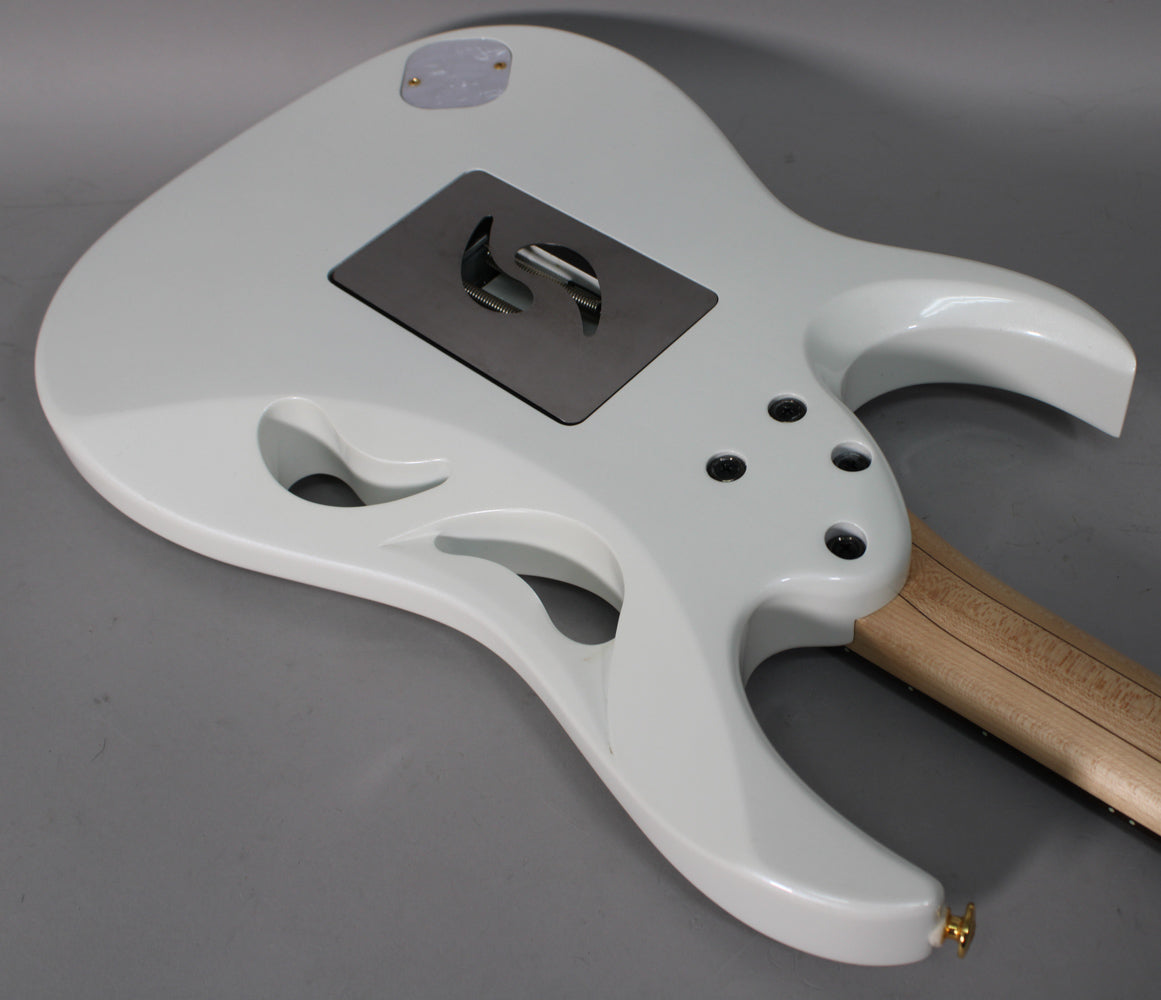 The back of a white electric guitar, angled from the lower left, shows a tremolo cavity and three carved "monkey grip" holes.