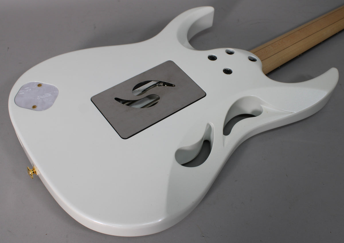 The back of a glossy white electric guitar, angled from the lower left, shows a metal tremolo spring cover and a pearloid control plate.