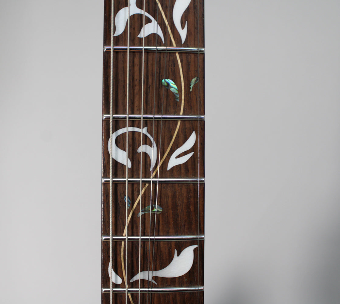Close-up of the dark rosewood fretboard with ornate white and iridescent green vine inlay, showing frets and strings.