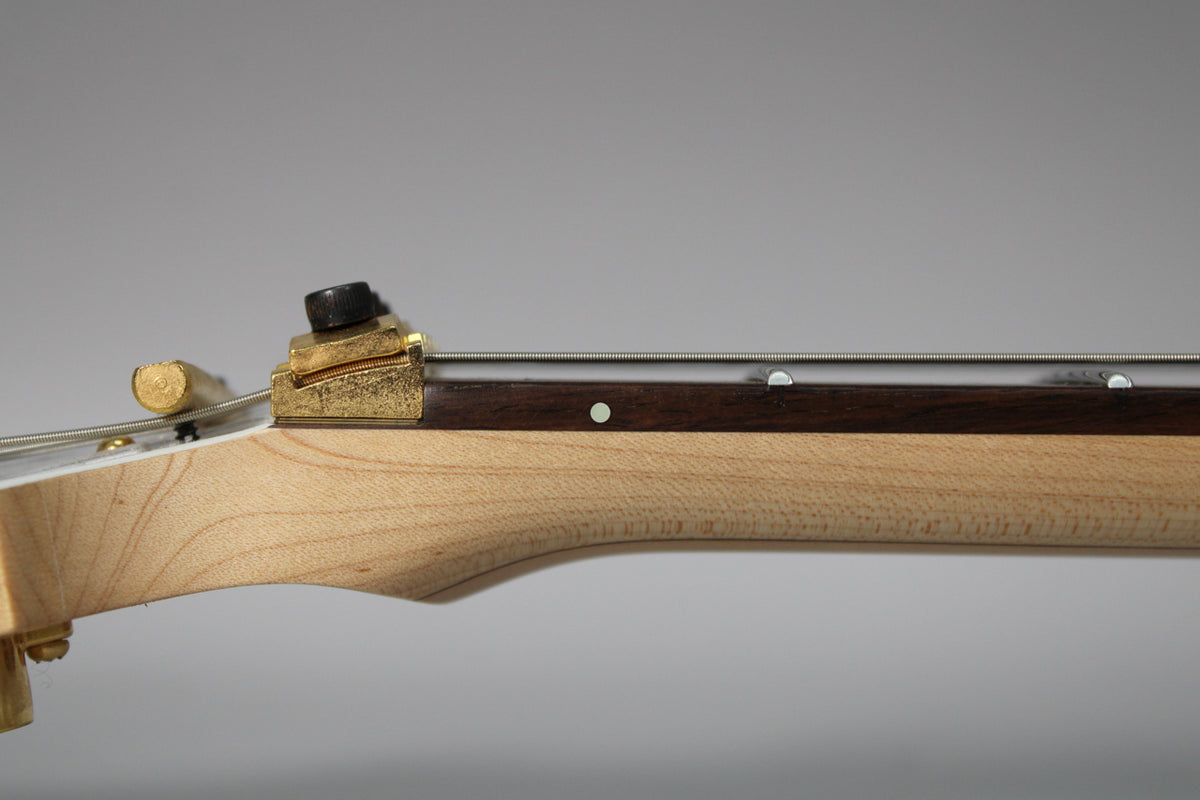 Close-up of the guitar's light wood neck and dark fretboard, showing a brass locking nut and string tree with light wear.