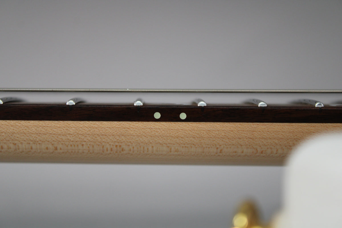 Close-up of the guitar's dark fretboard and light maple neck, showing two light green side dot markers and several frets.