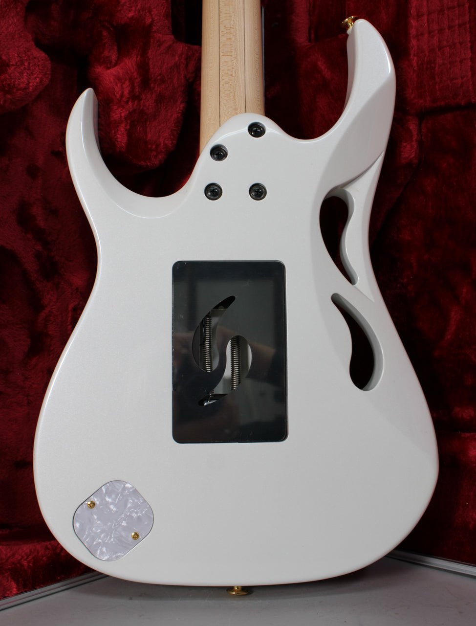 The back of a white electric guitar, showing the tremolo cavity, pearloid control plate, and a carved "monkey grip."