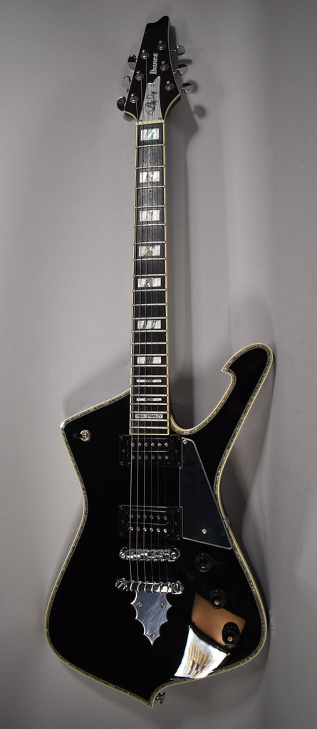Full-length, angled view of a glossy black electric guitar with a unique body shape, chrome hardware, and pearloid block inlays.