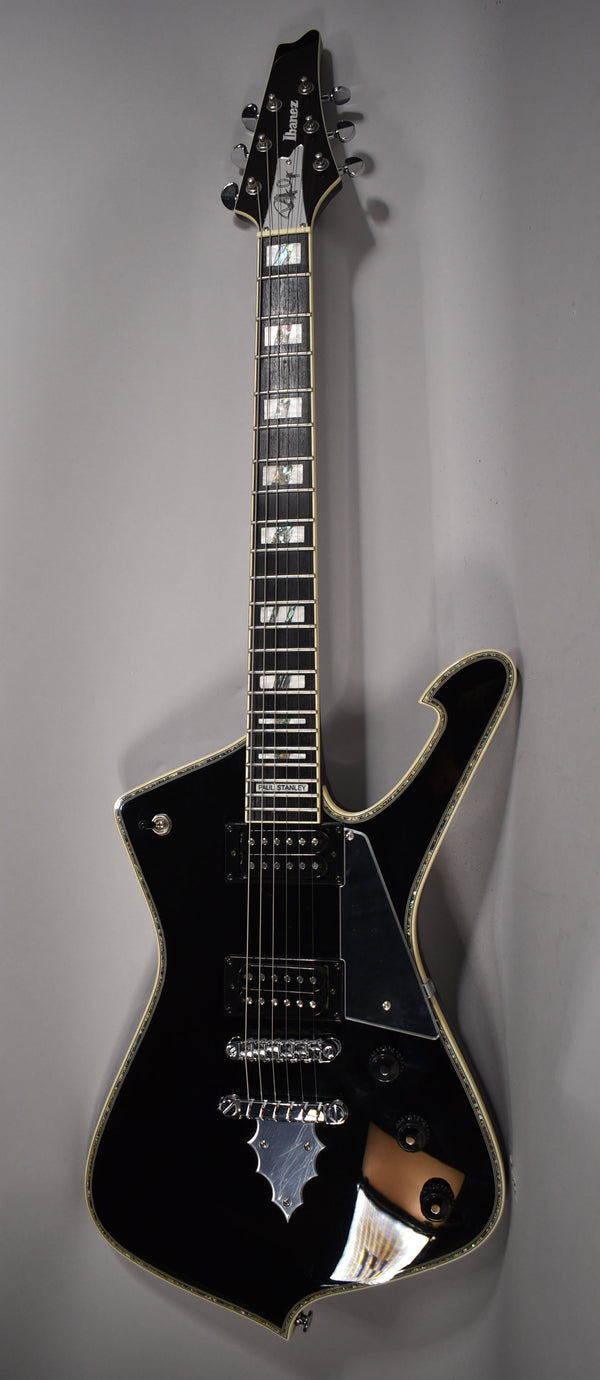 Full-length, angled view of a glossy black electric guitar with a unique body shape, chrome hardware, and pearloid block inlays.
