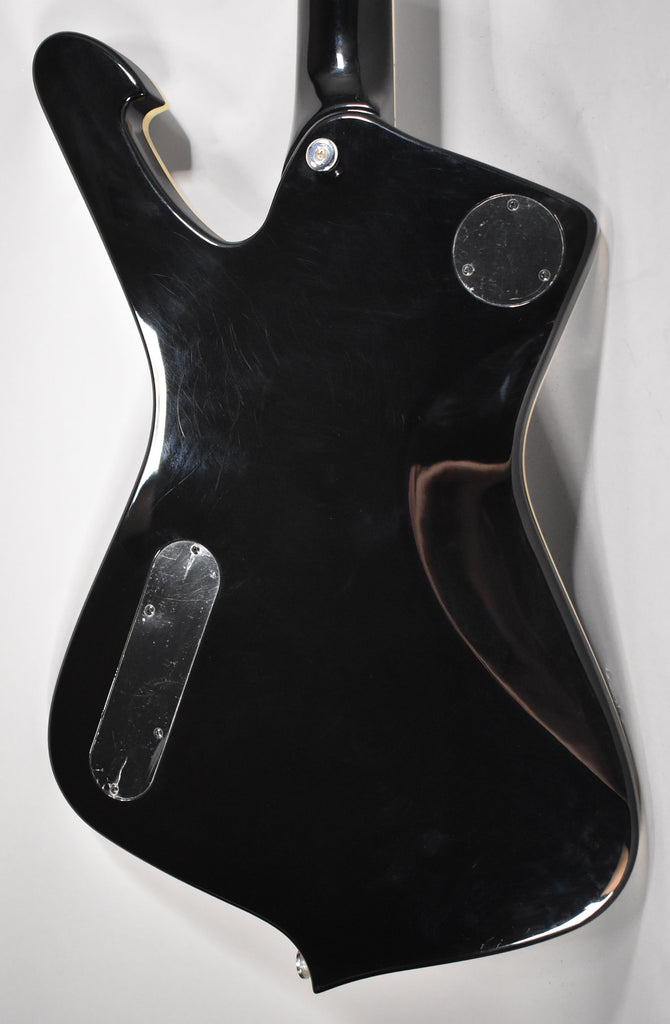 The guitar's glossy black back shows light surface scratches, with two silver control plates and a neck plate.