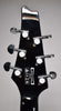 The guitar's glossy black headstock, viewed from the back, features six chrome tuners with white pearloid buttons and light surface scratches.