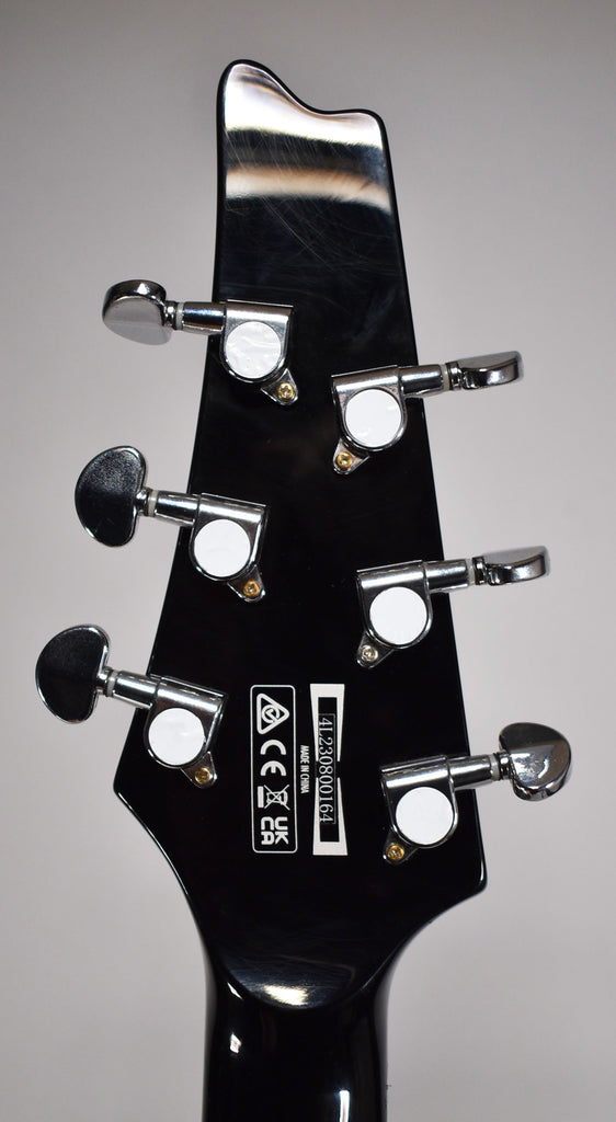 The guitar's glossy black headstock, viewed from the back, features six chrome tuners with white pearloid buttons and light surface scratches.