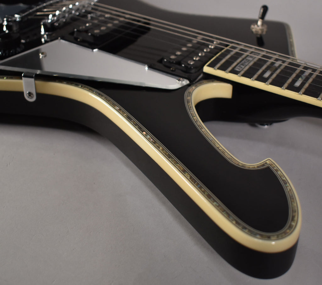 Close-up of the glossy black body, showing the cream binding with abalone inlay, chrome pickguard, and part of the fretboard.
