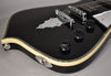 The glossy black guitar body, framed from the lower bout, features cream binding, three black control knobs, and a chrome bat-wing tailpiece.