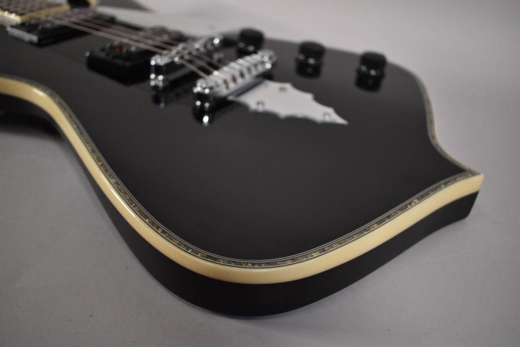 The black guitar body, with a cream and abalone binding, is angled to show the chrome bridge and tailpiece.
