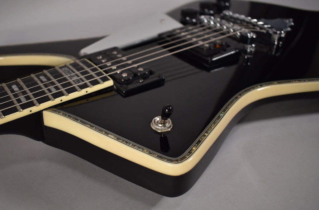 Close-up of the glossy black guitar body, showing cream binding with abalone purfling, a chrome toggle switch, and two humbucker pickups.