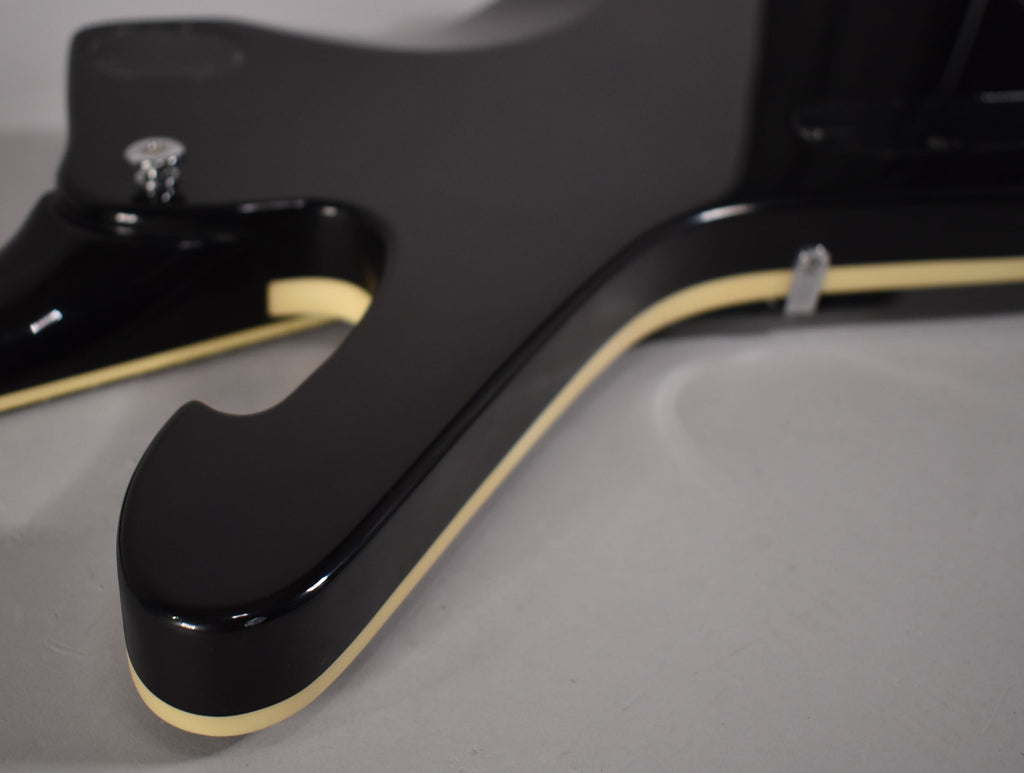 Close-up of the guitar's lower body, showing the glossy black finish and cream binding along the edges, with a strap button visible.