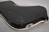 The glossy black guitar body's back shows a control cavity cover with scratches, a chrome output jack, and cream binding.
