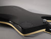 The guitar's glossy black body, with cream binding, is shown from the back, revealing a circular control plate and a chrome strap button.