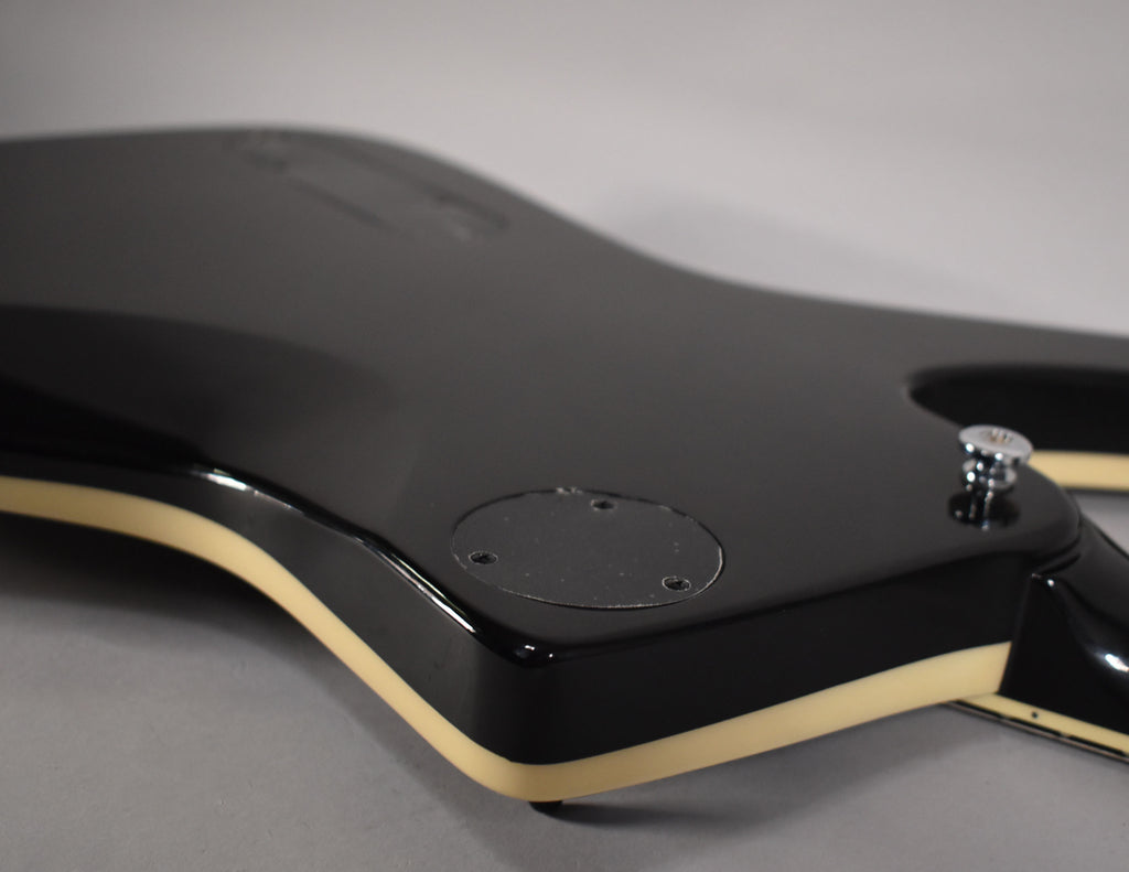 The guitar's glossy black body, with cream binding, is shown from the back, revealing a circular control plate and a chrome strap button.