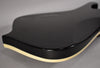 The guitar's glossy black body is angled, showing the upper bout and the cream binding along the curved edge.