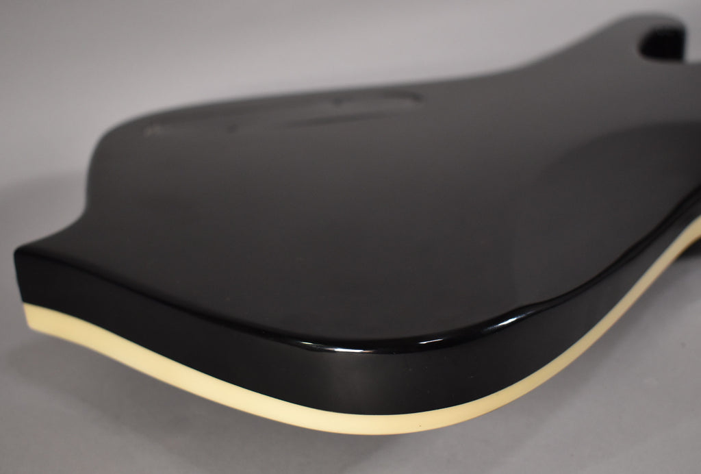 The guitar's glossy black body is angled, showing the upper bout and the cream binding along the curved edge.