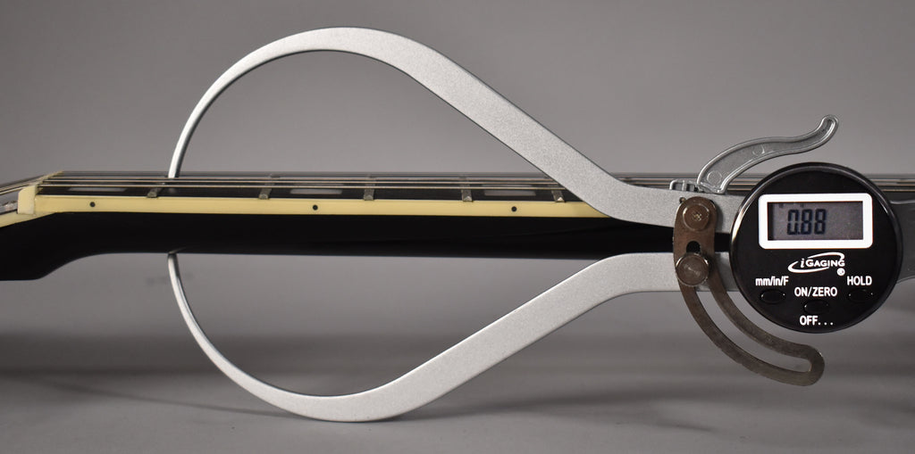 A digital caliper measures the neck relief of the black guitar, showing 0.88mm between the fretboard and strings.
