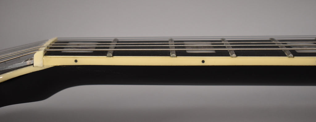 Close-up of the black guitar neck and fretboard from the side, showing cream binding, frets, and side dots.