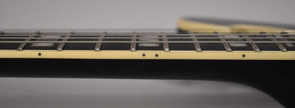 A close-up of the black guitar's fretboard, showing cream binding, dot side markers, and block inlays on the dark fretboard.