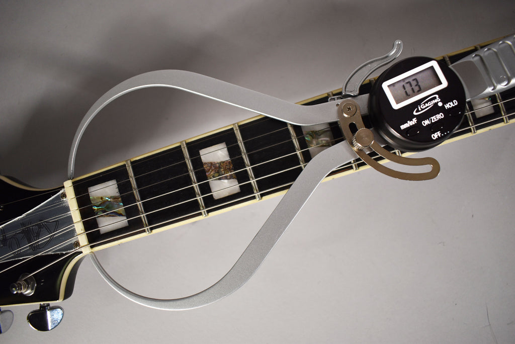 A digital caliper measures the black fretboard with pearloid block inlays, showing a reading of 1.73.
