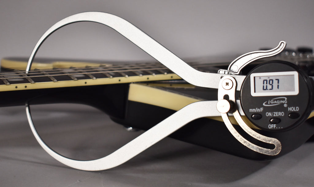 A digital caliper measures the string height at the 12th fret of the black guitar neck, displaying "0.97".
