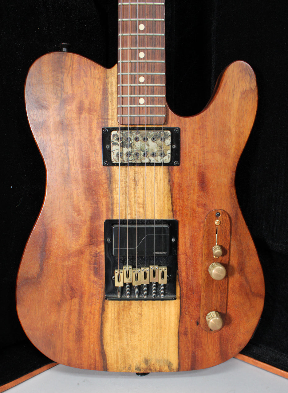 Full front view of a T-style guitar with a natural wood finish, two humbucker pickups, and three brass control knobs.