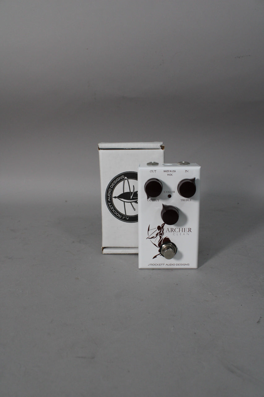 A white guitar pedal with three dark brown knobs and a silver footswitch, angled to show the top and right side, with its box behind it.