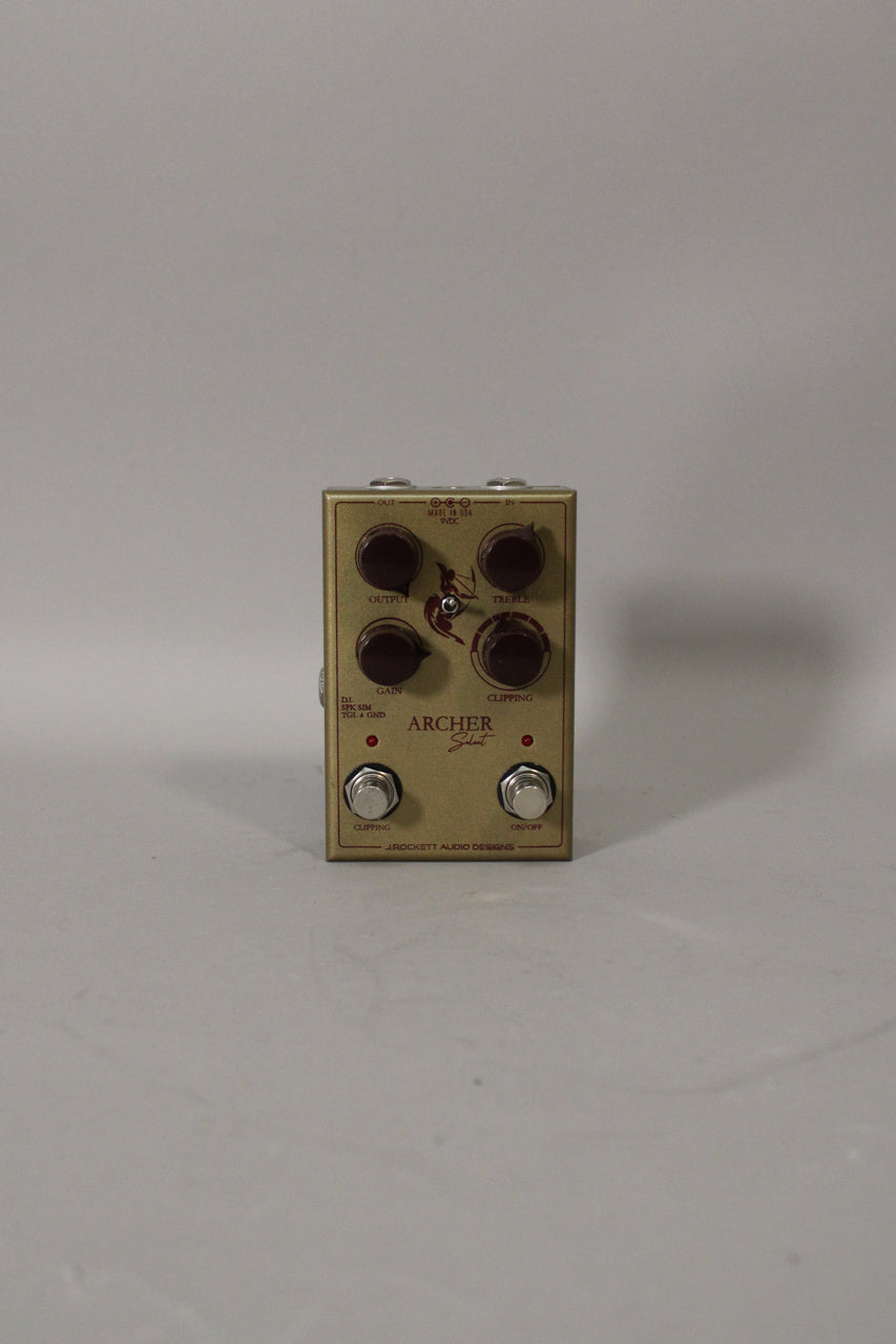A gold guitar pedal with four dark brown control knobs, two silver footswitches, and a red archer graphic.