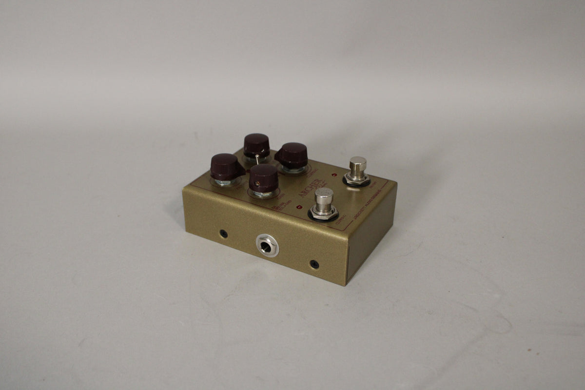 A gold-colored guitar pedal with five dark brown knobs and two silver footswitches, viewed from the front-right.
