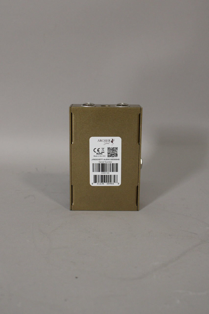 The gold-colored pedal is viewed from the rear, showing a white product label with a barcode and two silver jacks on top.