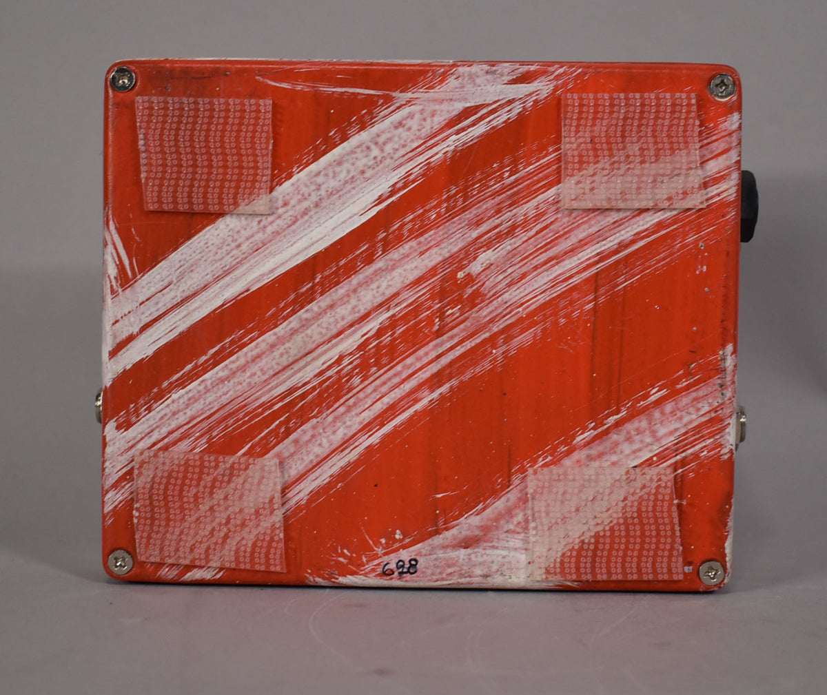 The pedal's orange base is covered in white brushstrokes and four clear velcro pads, with "628" written in black.