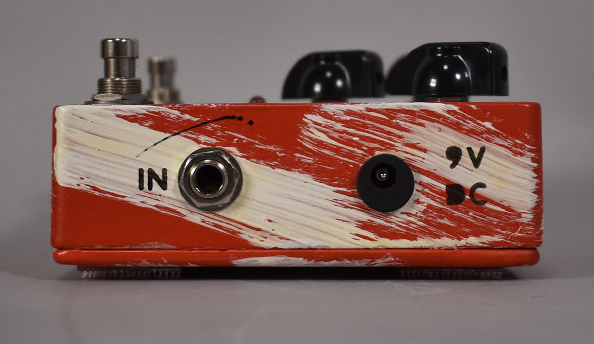 The right side of the red pedal, painted with white streaks, shows the "IN" jack and a 9V DC power input.