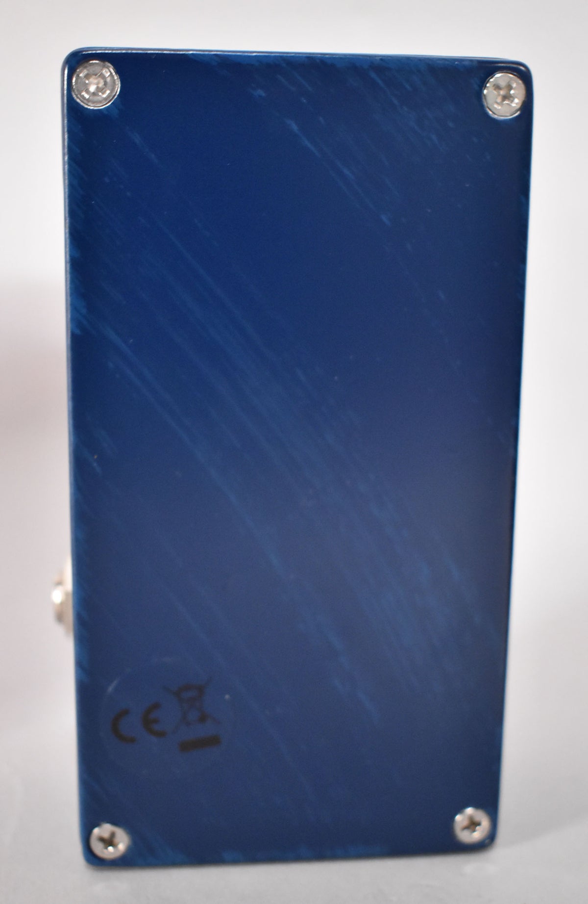 The dark blue pedal's bottom plate is shown, secured by four silver Phillips head screws, with light scuffs and a CE mark.
