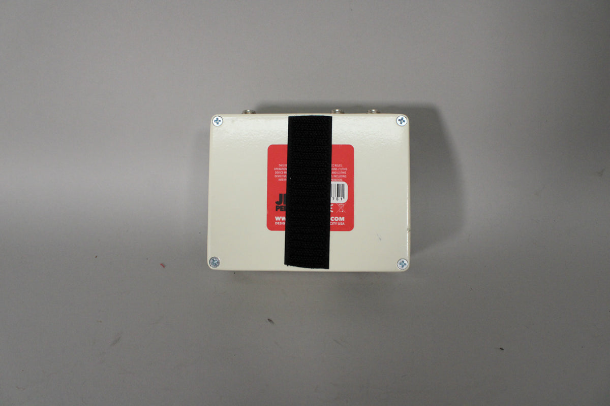 The pedal's off-white underside is visible, with a red label and black hook-and-loop tape across the center.